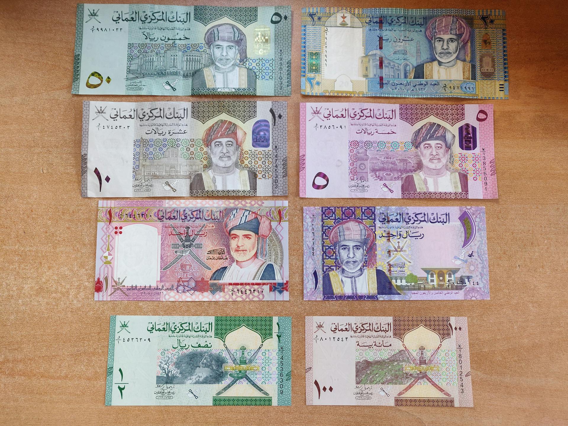 A collection of Omani Rial banknotes arranged on a wooden surface, showcasing various denominations.