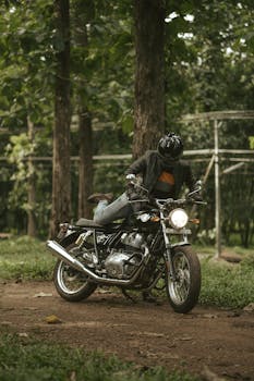 A motorcyclist in leather gear rides through a dense forest trail, highlighting adventure and exploration.