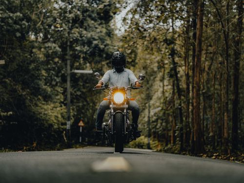 Free A motorcyclist rides along a tranquil road through a lush green forest, showcasing adventure and freedom. Stock Photo