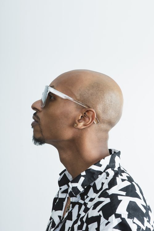 Free Profile portrait of a bald man wearing sunglasses and a geometric patterned shirt against a white background. Stock Photo