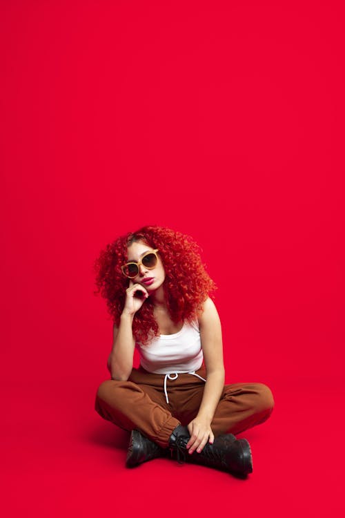 Woman with Curly Hair Sitting Cross-legged on Ground on Red Background