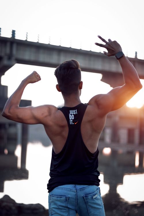 Free Muscular man posing with peace sign near bridge during sunset, showcasing fitness and strength. Stock Photo