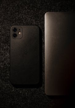 Close-up of a black smartphone and laptop on a textured dark background. Perfect for technology themes.