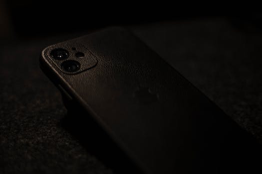 Close-up image of a smartphone with a dark leather case in low lighting.