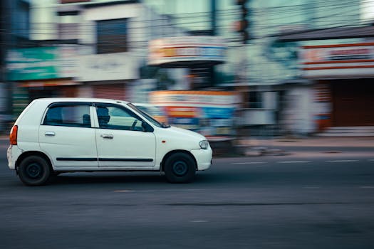 A white car speeds past on a city street, captured with motion blur, showcasing urban transportation and movement.
