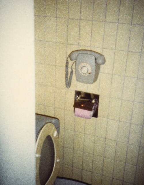 A Telephone and Toilet Paper on a Tiled Restroom Wall