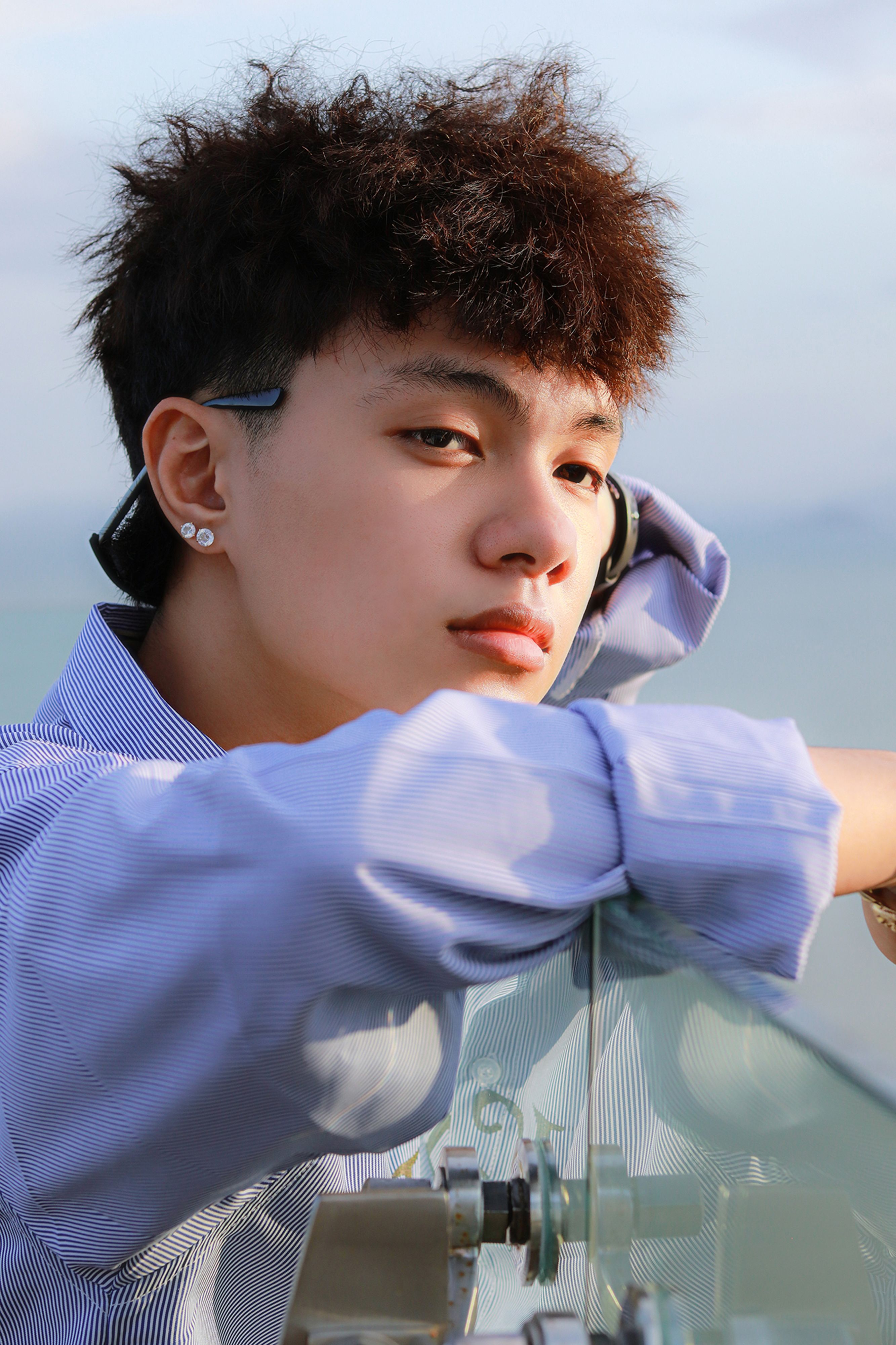 Young man with headphones reflecting by a glass railing outdoors, casual style.