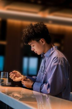 Teenager in a blue shirt adjusting wristwatch at a sleek bar setting.