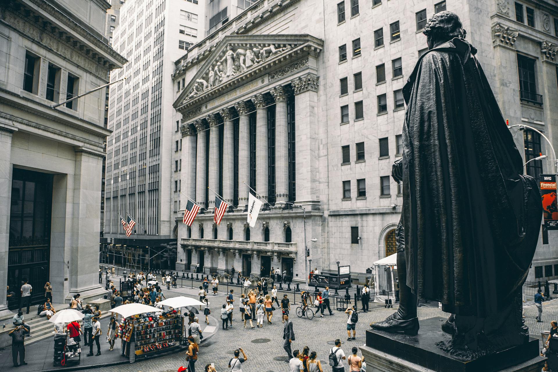 View of the New York Stock Exchange with busy street life and iconic statues.