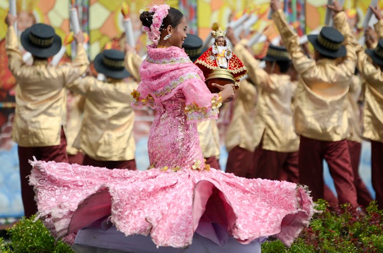 A Woman In A Pink Dress Carrying An Image Of The Santo Niño