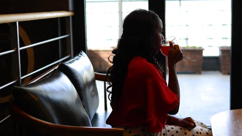 Frau, Die Rote Langärmelige Bluse Sitzt Und Flüssigkeit Trinkt