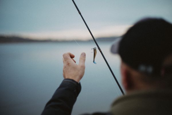 Pescador ajustando a isca na vara à beira do lago