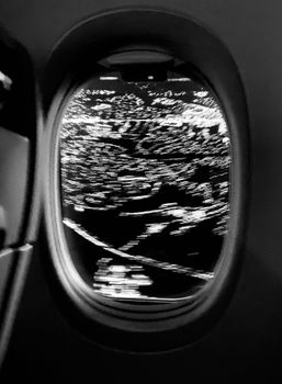 Black and white view through airplane window showing night city lights below.