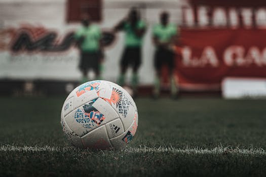 A detailed view of a soccer ball on a grass field with players blurred in the background.