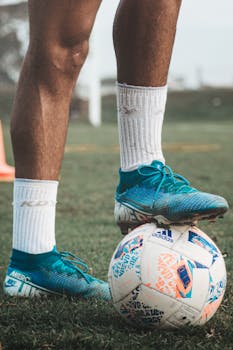 Vertical shot of soccer player's feet in blue cleats with ball on grassy field.