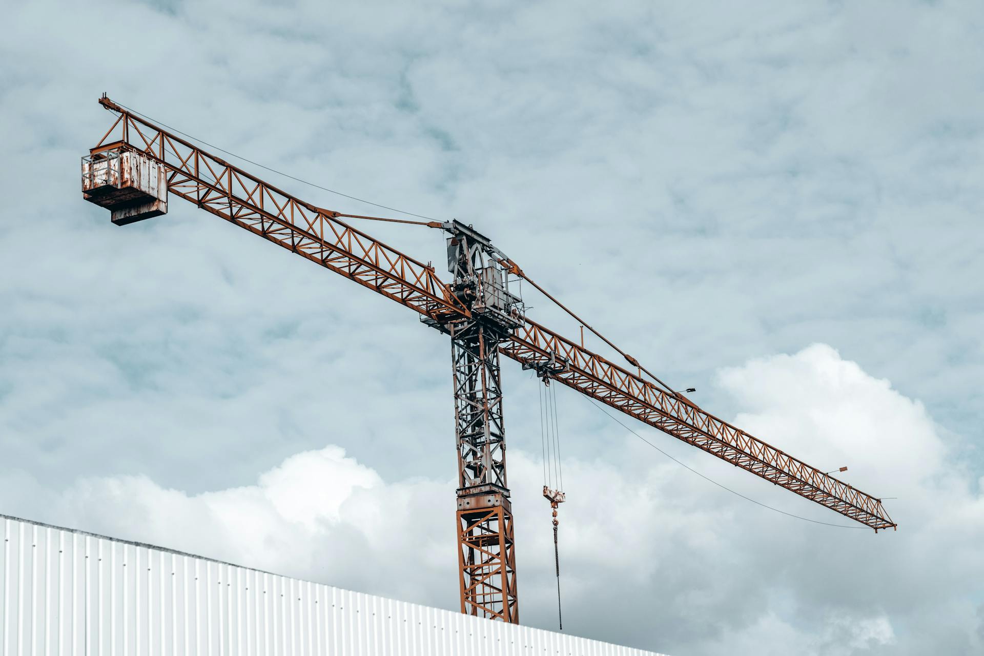 A towering crane at a construction site with a dramatic cloudy sky in the background.