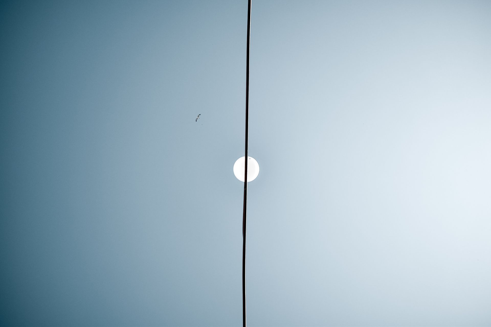 A single electric wire intersects the moon against a blue sky, creating a minimalist design.
