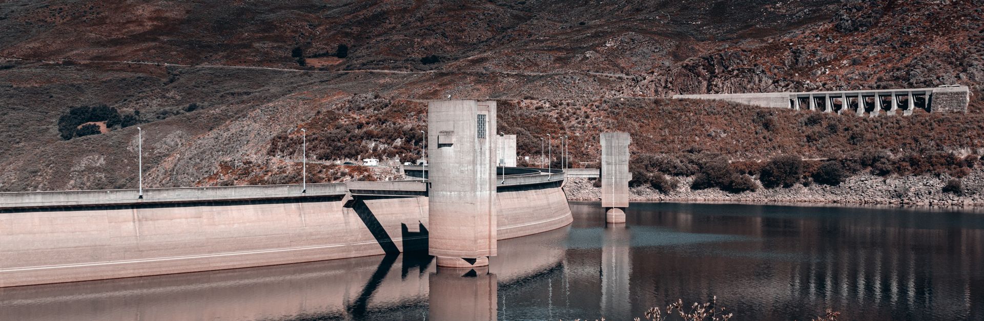 Explore a serene dam and reservoir set against a backdrop of rugged mountains and calm water reflect