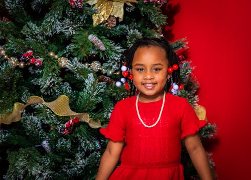 A Girl in Red Dress Standing Beside the Christmas Tree