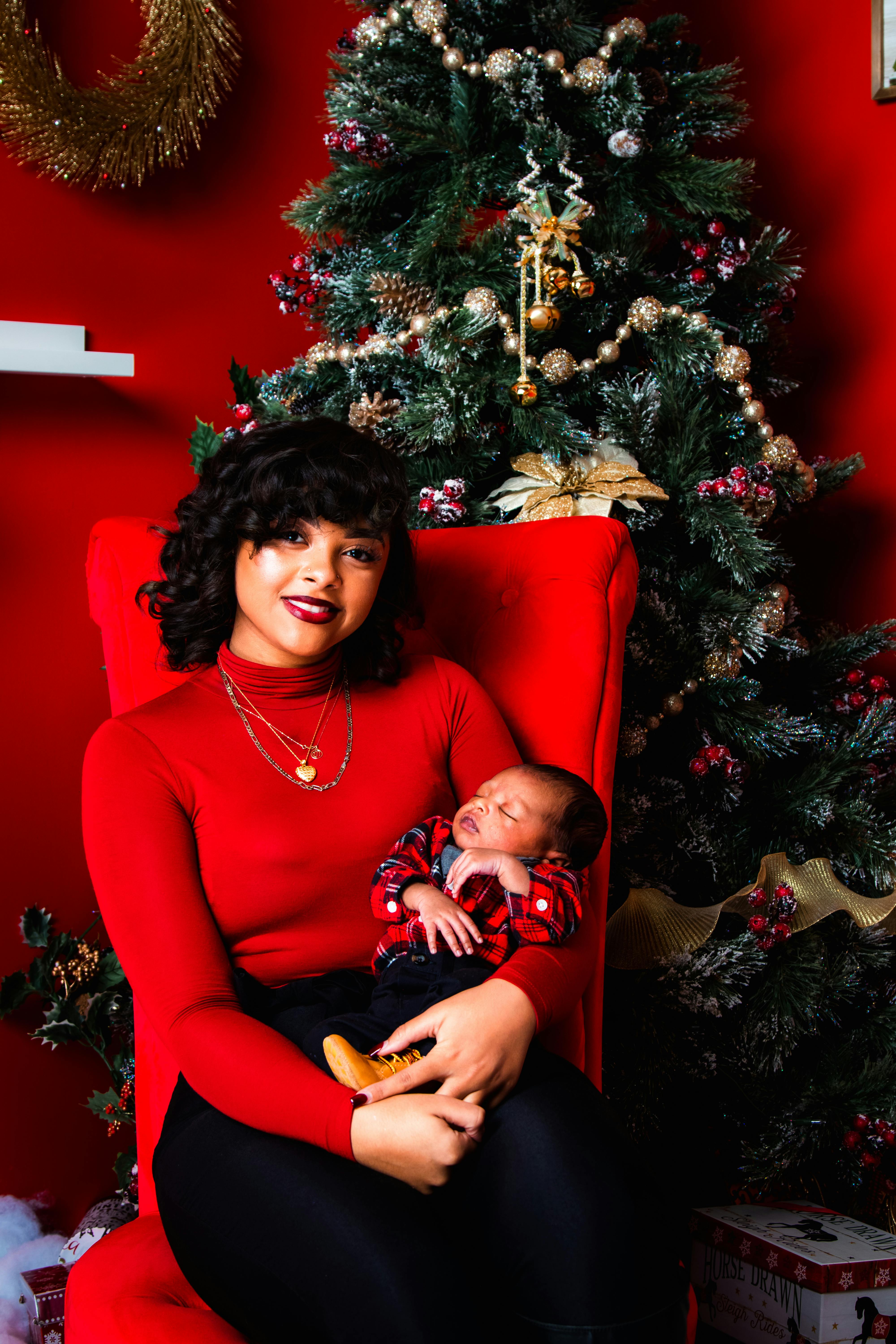 woman carrying a baby while sitting beside the christmas tree