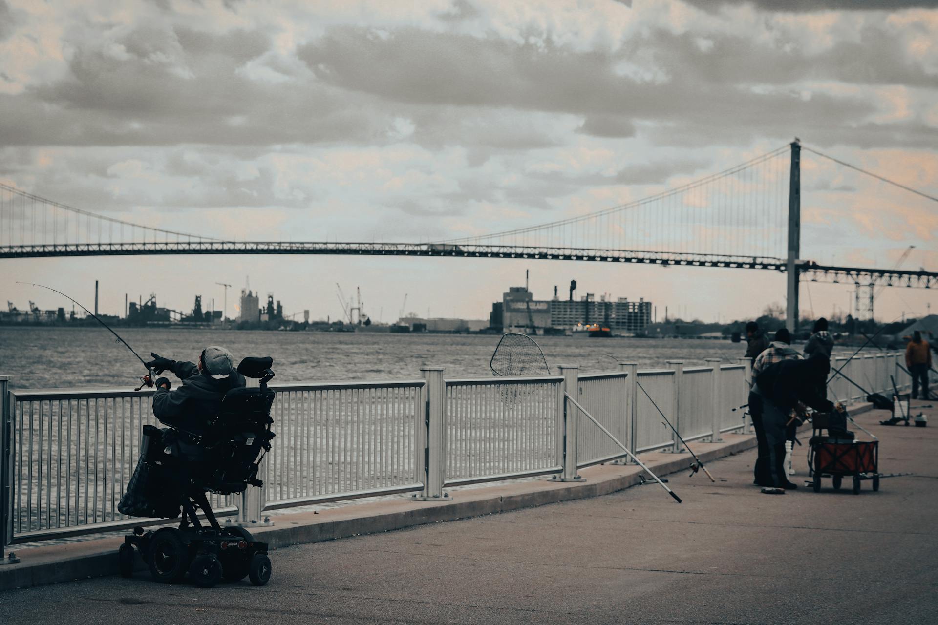 Fishermen enjoying a cloudy day by the river near the iconic Ambassador Bridge in Detroit.