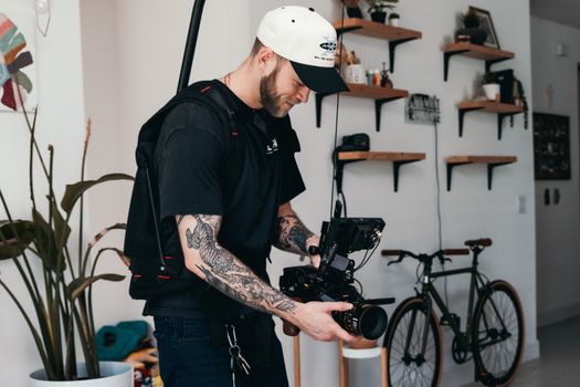 A male filmmaker adjusts professional camera equipment indoors, surrounded by decor and a bicycle.
