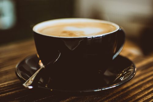 Free Warm espresso with cream foam served in a black ceramic cup on wooden table. Stock Photo