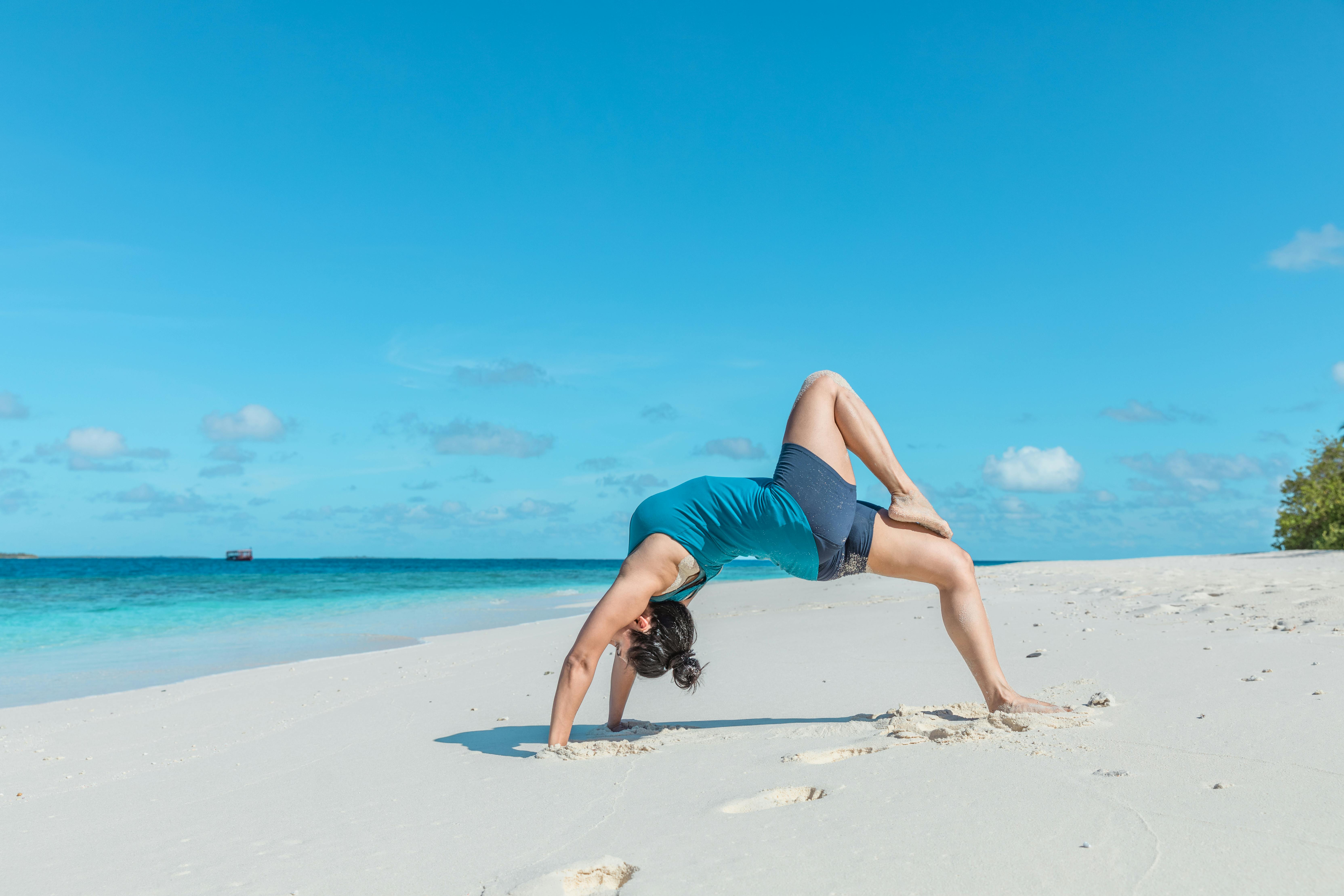A woman performs yoga on a pristine beach in the Maldives, under a clear blue sky.