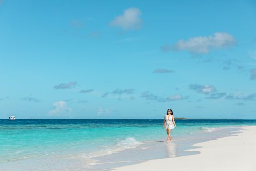 Free Woman walking along a beautiful white sandy beach in the Maldives under a bright blue sky. Stock Photo