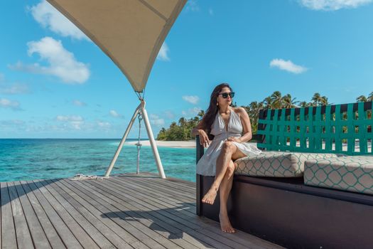 Woman sitting on a resort terrace by the ocean, enjoying a sunny tropical day.