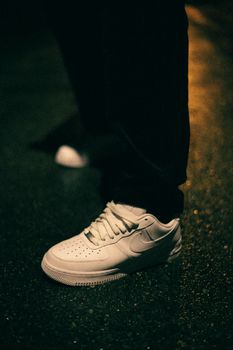 Vertical shot of a white sneaker on wet asphalt illuminated by streetlight at night. Perfect for fashion and lifestyle themes.