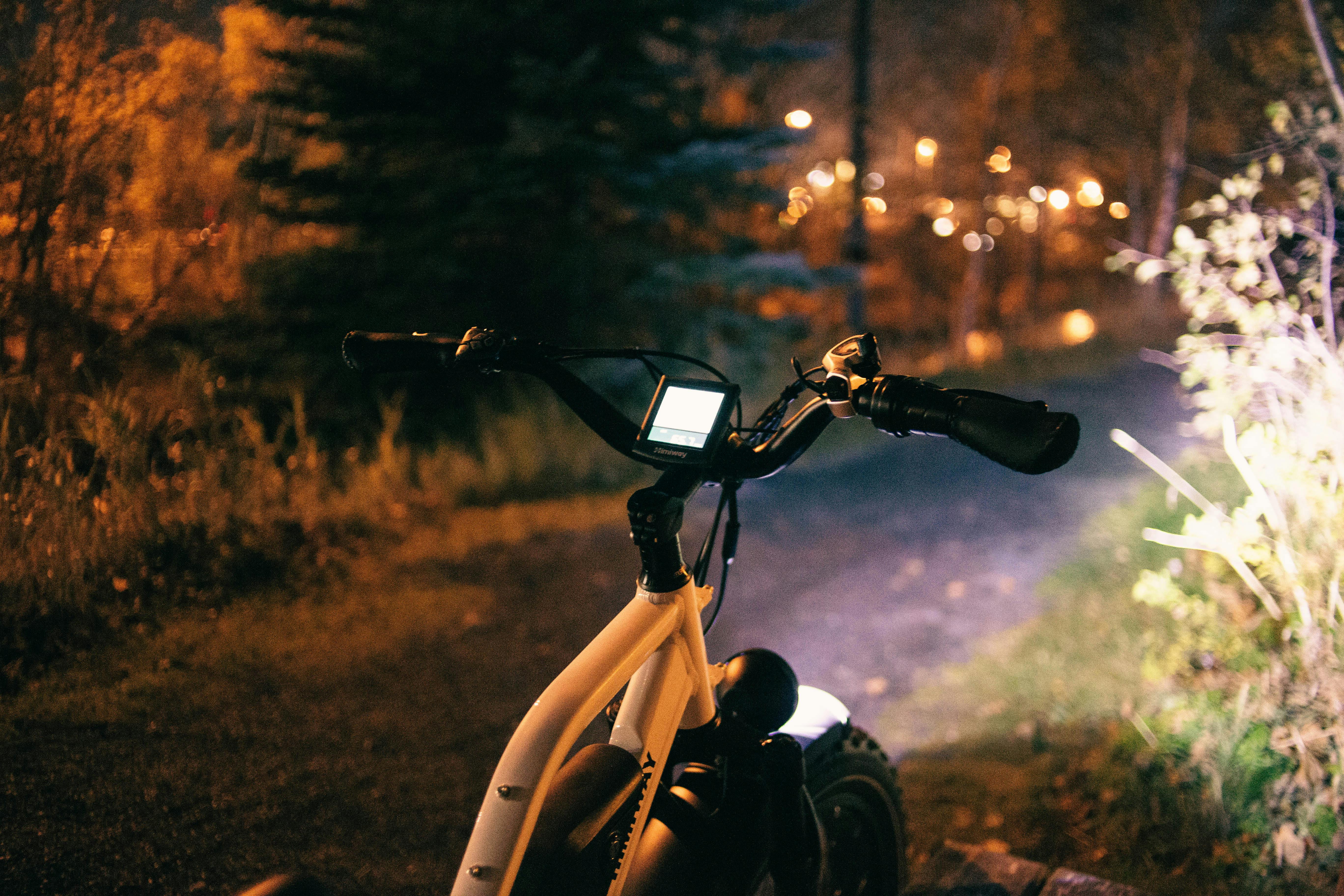Bicycle with a headlight illuminating a forest path during a nighttime ride.