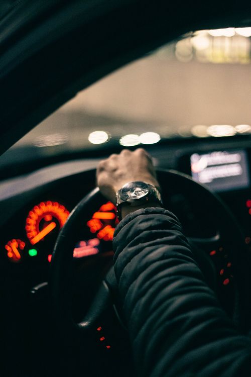 Free A person driving a car, showcasing a close-up of a hand on the steering wheel inside a vehicle at night. Stock Photo