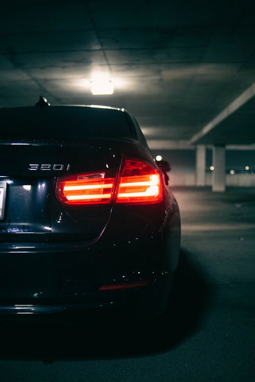 Free Close-up of a black car's rear light glowing in a dark parking garage. Stock Photo