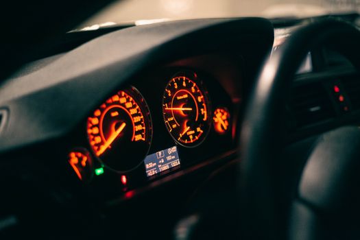 Close-up view of an illuminated car dashboard with glowing gauges at night.