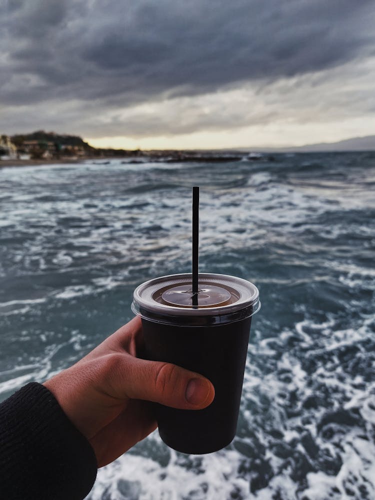 Man Hand Holding Takeaway Cup On Ocean Background