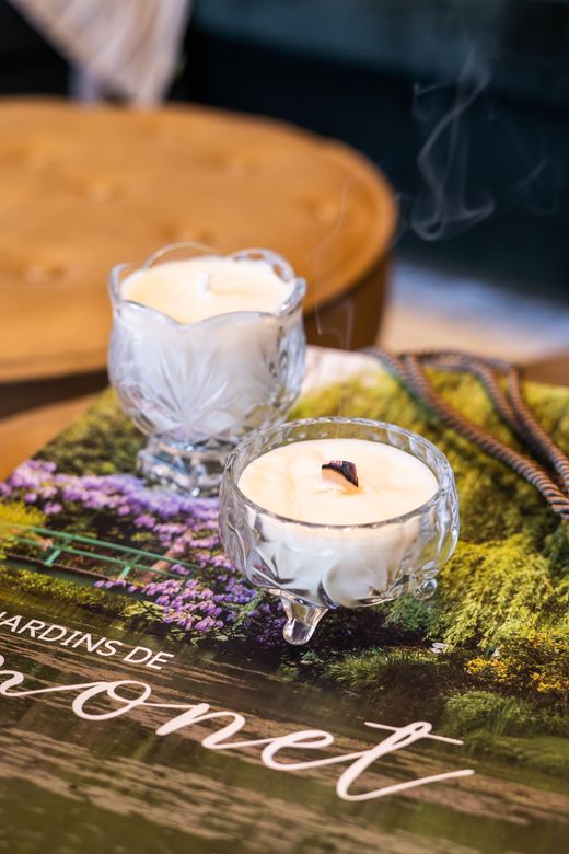 Two handmade candles in glass holders sitting on a stack of decorative books