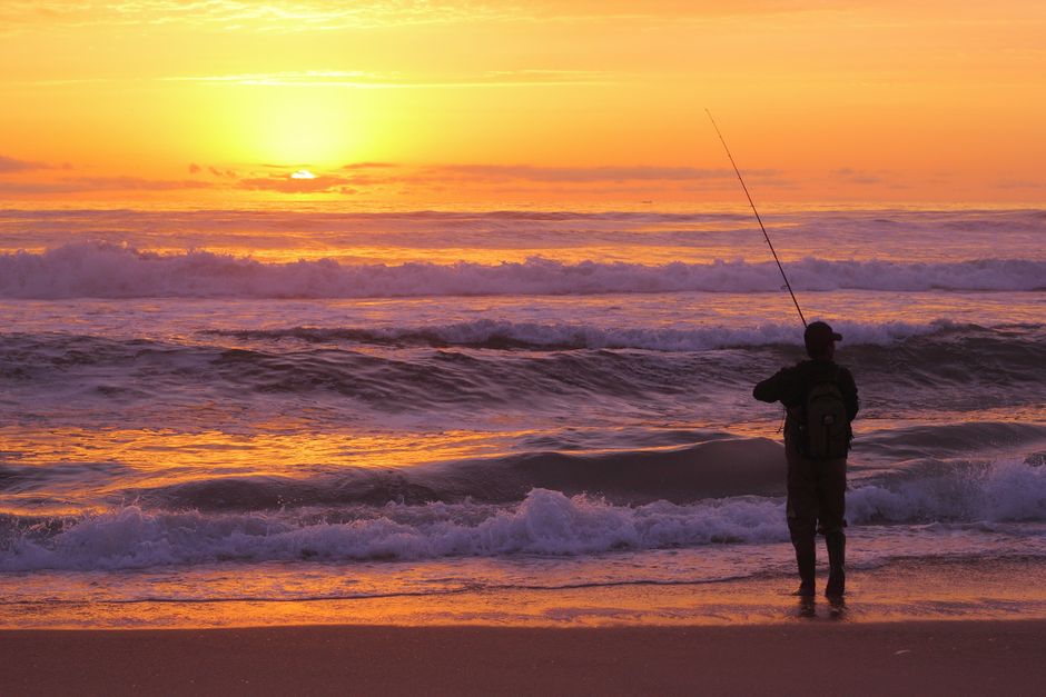 夕暮れの堤防で釣りをする人のシルエット