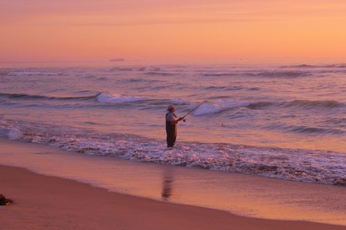Free A serene scene of a man fishing at sunset on the beach of El Tabo, Chile. Stock Photo