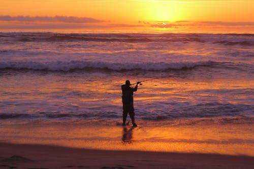Free Man in Black Jacket Standing on Seashore during Sunset Stock Photo