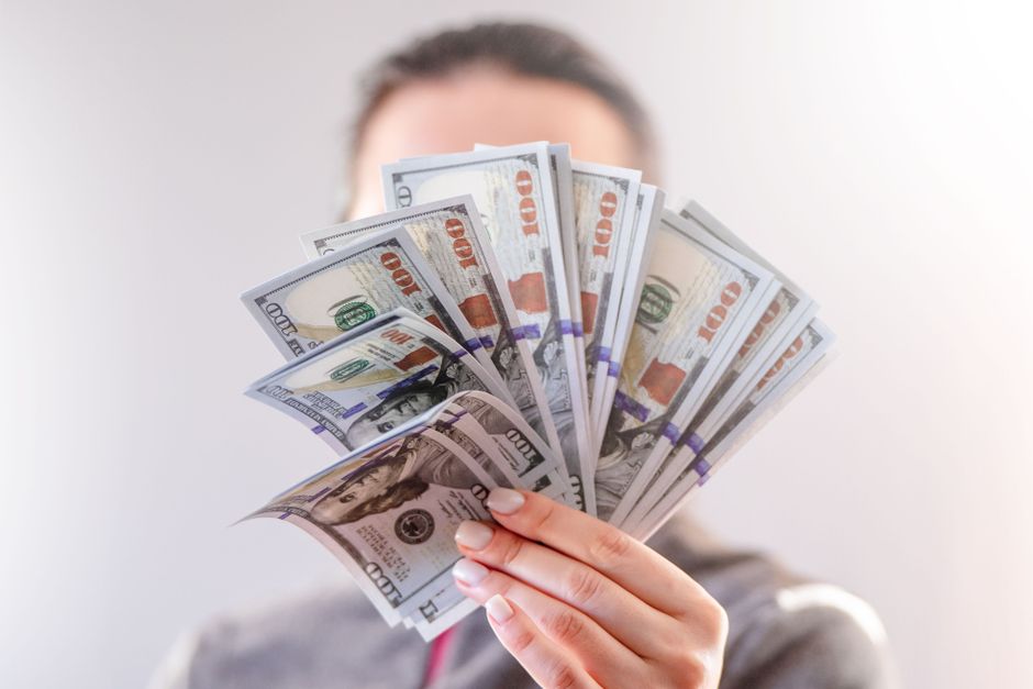 A close-up of a person holding a fan of US dollar bills, signifying wealth and financial success.