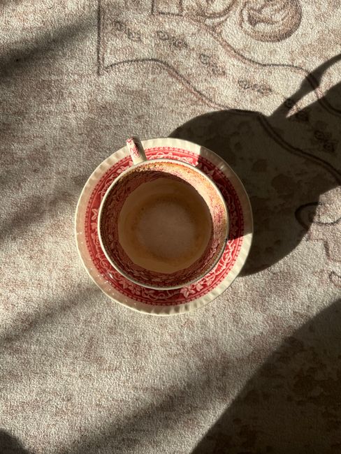 An elegant ornamented coffee cup sits empty on a matching plate, viewed from above.