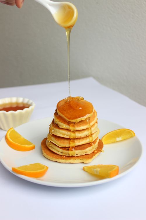 Free Tall stack of fluffy pancakes drizzled with honey and garnished with orange slices, perfect breakfast treat. Stock Photo