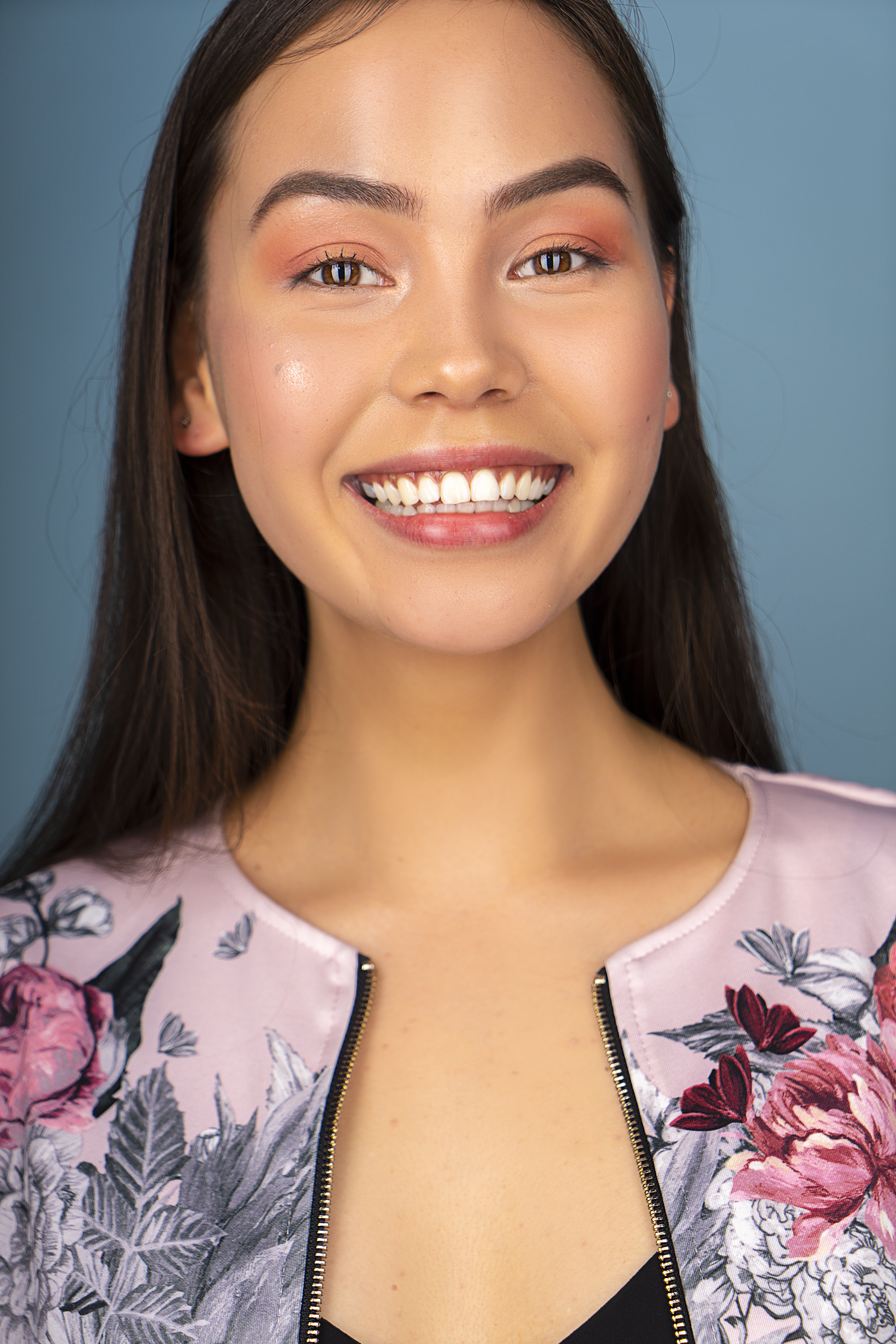 Close-up portrait of a smiling woman wearing floral jacket against blue background.