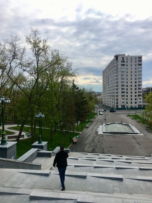 Free A view of a man walking in a park in Kharkiv, Ukraine, with a high-rise building and overcast sky. Stock Photo