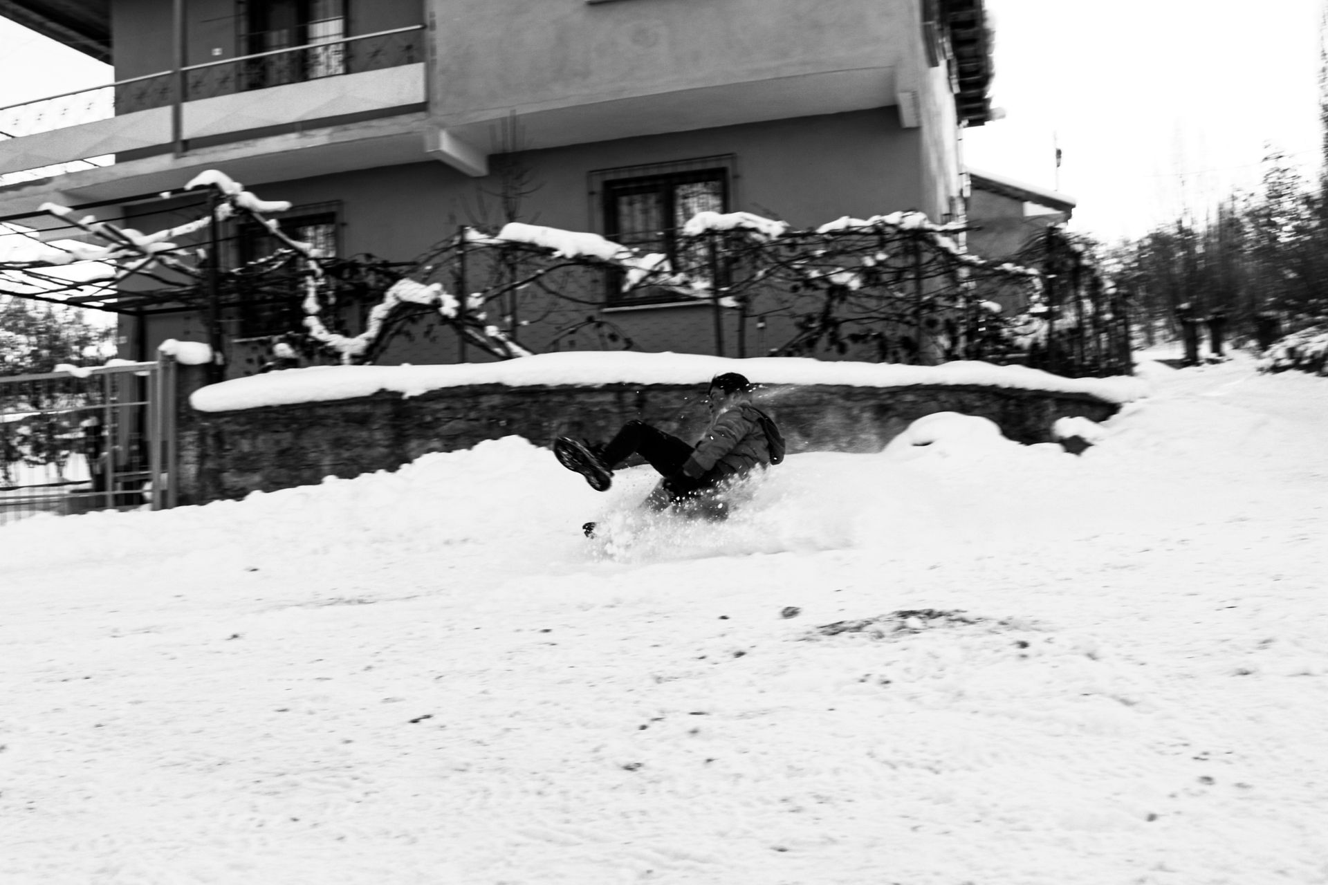 A person sliding down a snowy hill in winter, captured in monochrome.