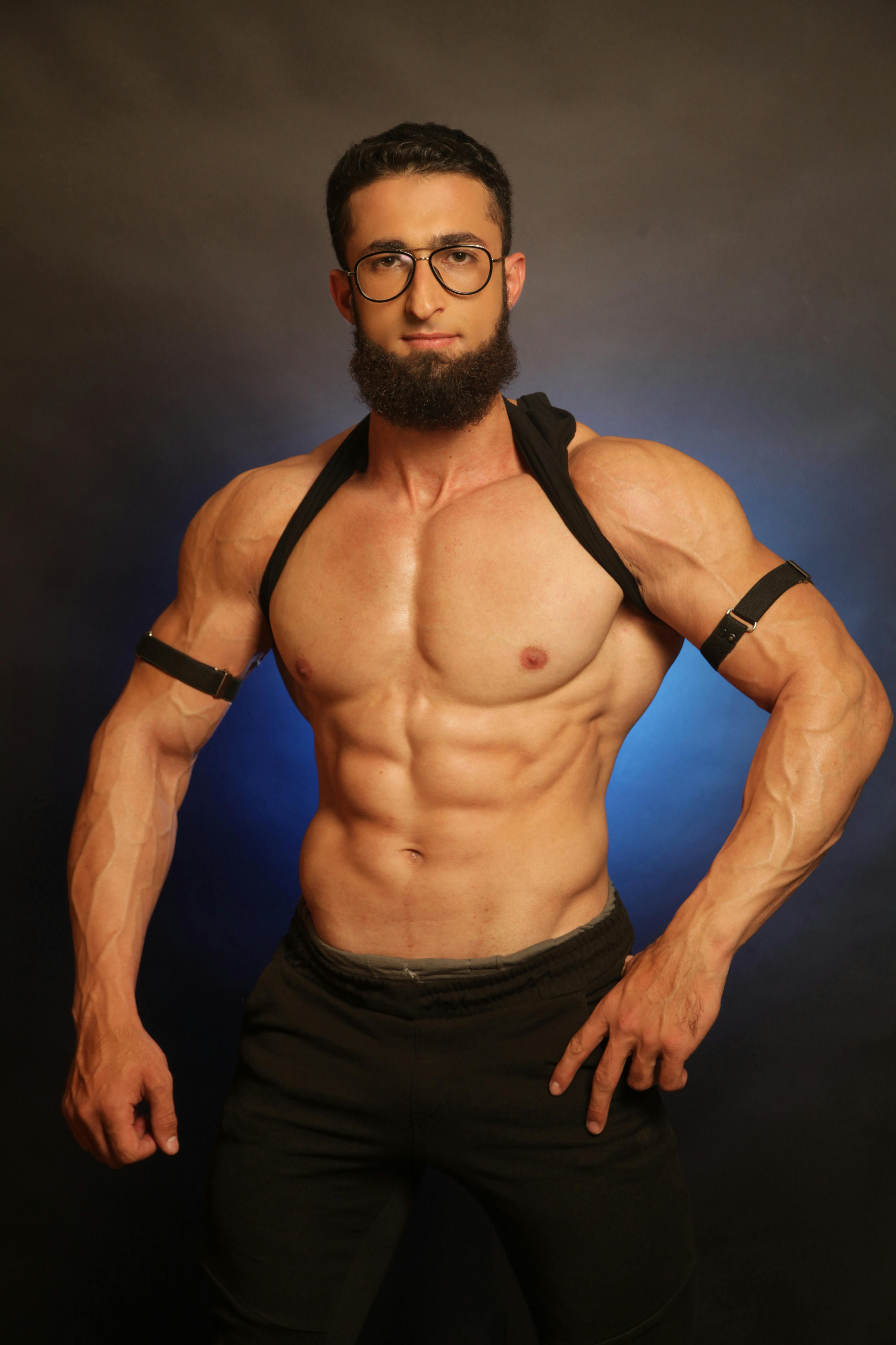 A muscular man posing shirtless with eyeglasses, showcasing fitness and strength.