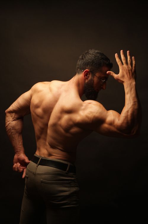 Free Rear view of a muscular man flexing in dim studio lighting, showcasing back muscles. Stock Photo