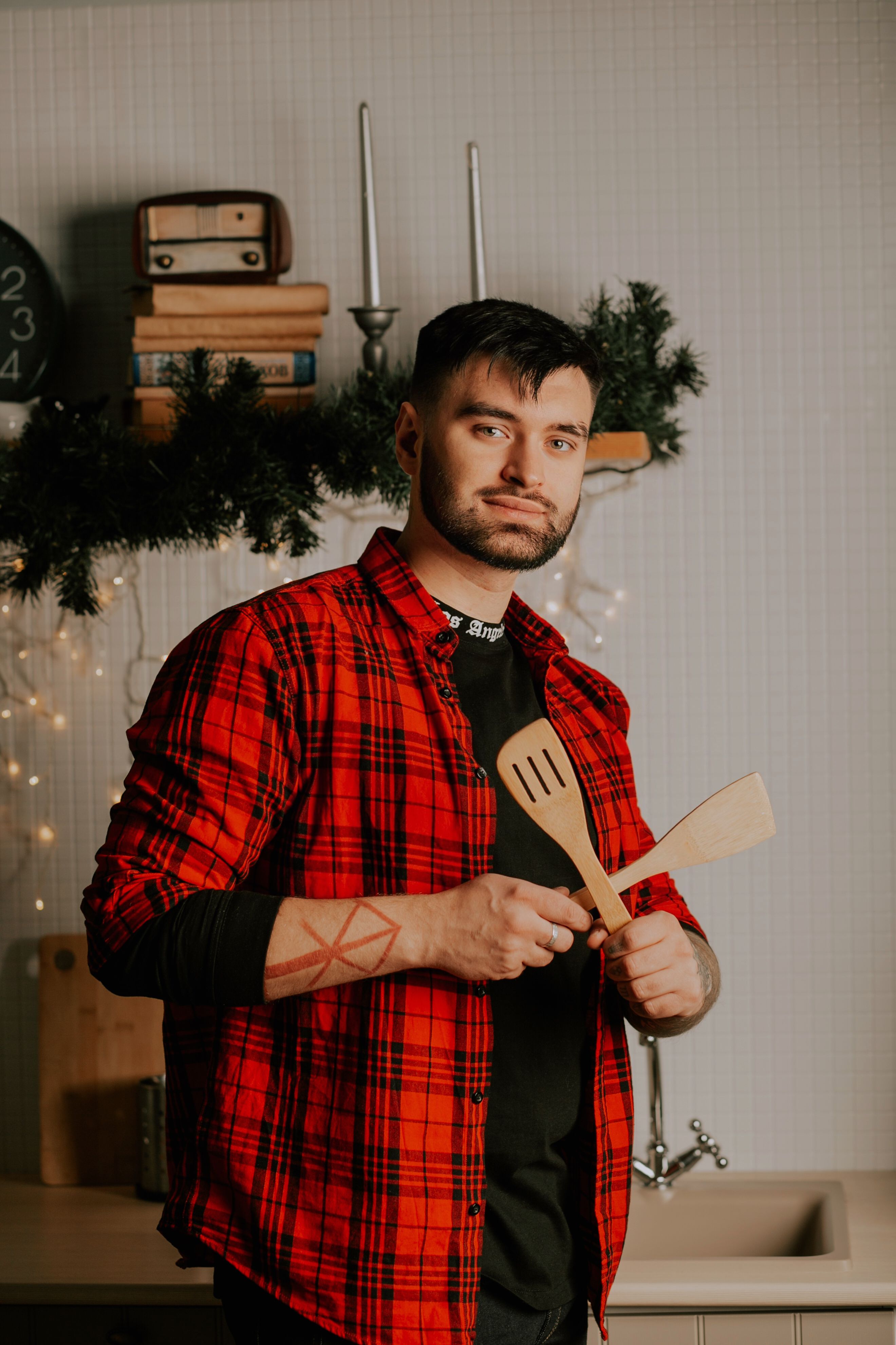 Young man in home kitchen holding wooden utensils, decorated for holidays