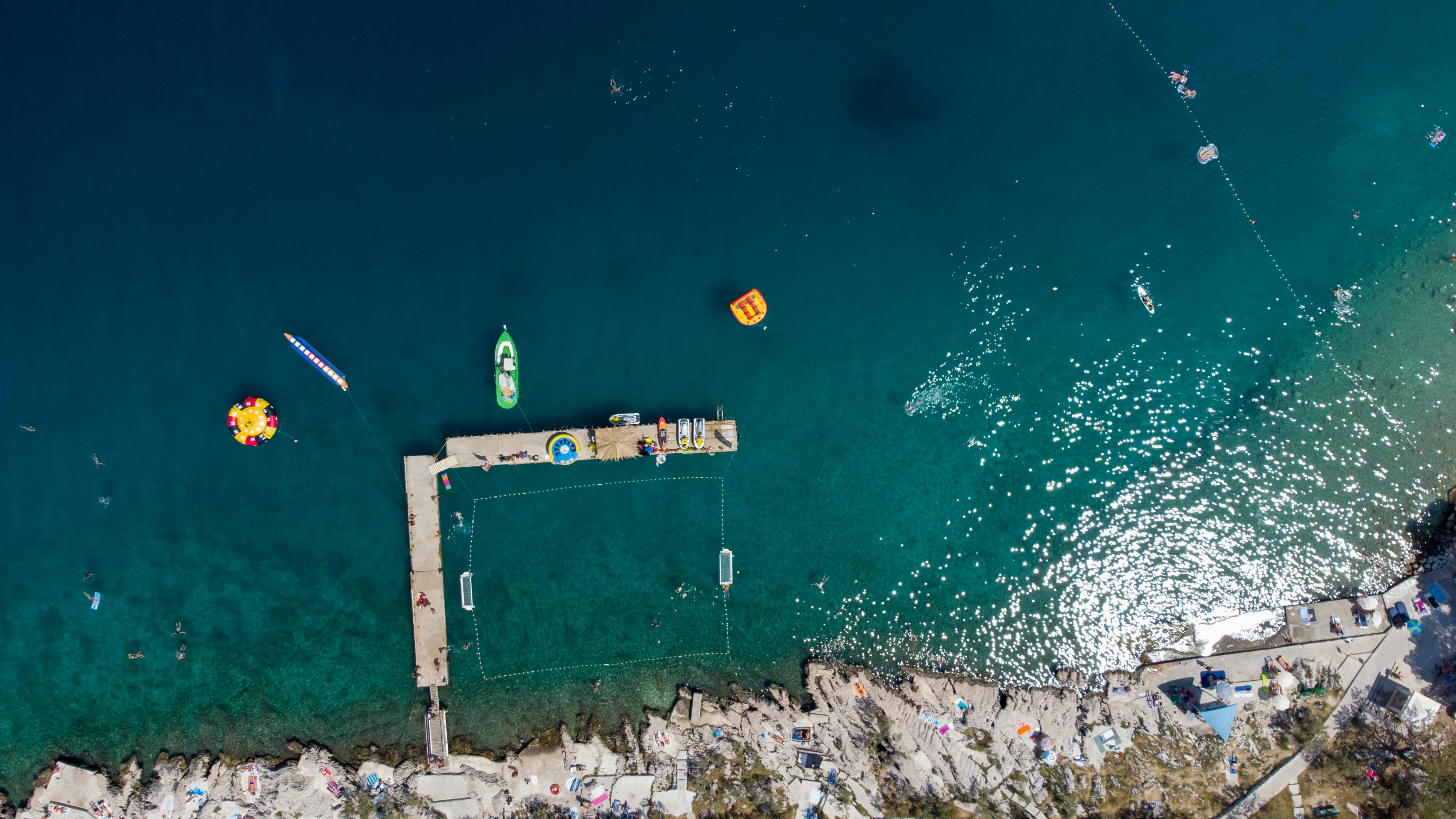 Explore a stunning aerial view of a Croatian pier and clear blue sea, capturing vibrant summer activities.